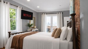 Ein Schlafzimmer mit Bett, einem an der Wand montierten Fernseher, einem Fenster und Blick auf die Stadt.