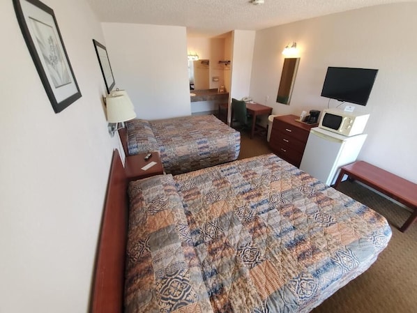 A hotel room with two beds, a desk, a chair, a TV, a microwave, and a dresser.