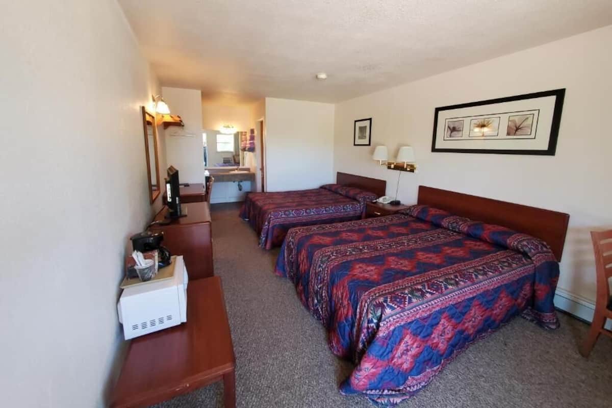 Habitación de hotel con tres camas, un escritorio, una silla y una mesita de noche con lámpara.