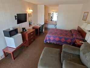 A hotel room with a bed, a desk with a chair, a television, a microwave, and a small refrigerator.