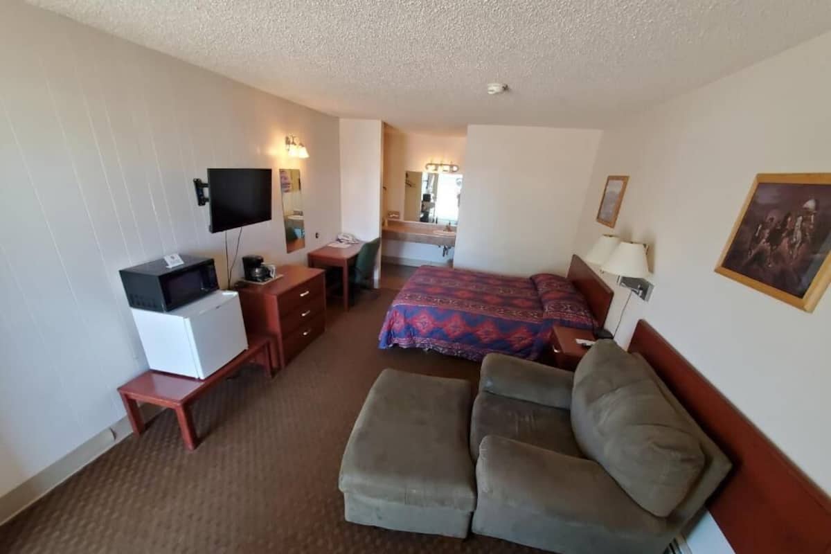 Una habitación de hotel con cama, sofá, escritorio con computadora, televisor y microondas.