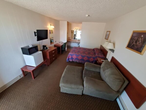 A hotel room with a bed, a sofa, a desk with a computer, a TV, and a microwave.