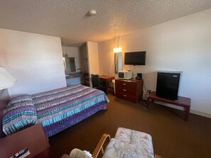 A hotel room with a bed, a desk, a television, and a microwave.