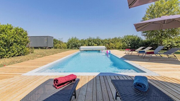 Une piscine avec une terrasse en bois, des chaises longues et un espace abrité.