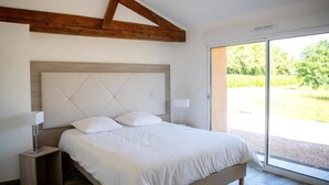 Une chambre avec un grand lit, des poutres en bois, une fenêtre et une vue sur la verdure.
