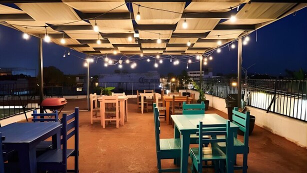 Un espace extérieur aménagé en terrasse, avec des tables et des chaises, des guirlandes lumineuses et une vue sur le paysage urbain au crépuscule.