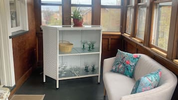 A cozy room with a white sofa, a small white table, a wicker basket, and a glass cabinet with wine glasses.