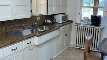A kitchen with white cabinets, a granite countertop, a coffee maker, and a window with a view of greenery.