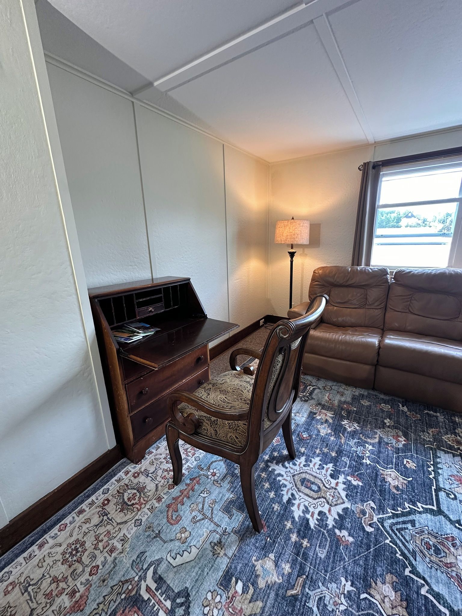 A room with a wooden desk, a leather sofa, and a patterned carpet.