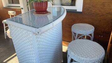 A glass-top bar table with wicker chairs, a potted plant, and a window in the background.