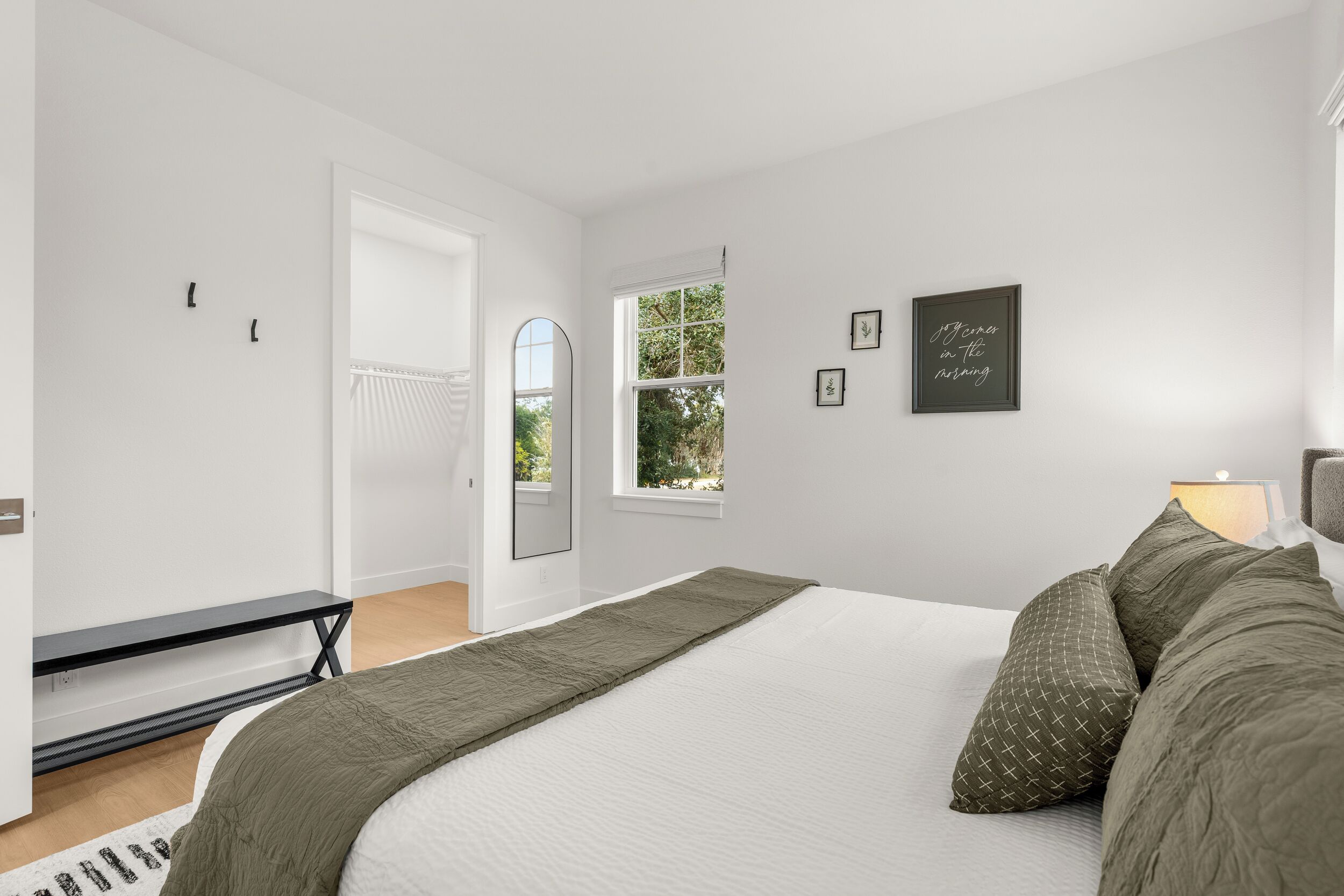 A bedroom with a bed, a bench, a window, and a door.