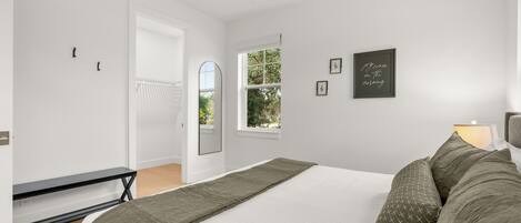 A bedroom with a bed, a bench, a window, and a door.