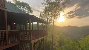 Eine Holzhütte mit einem Balkon, der auf ein bewaldetes Tal und Berge blickt.