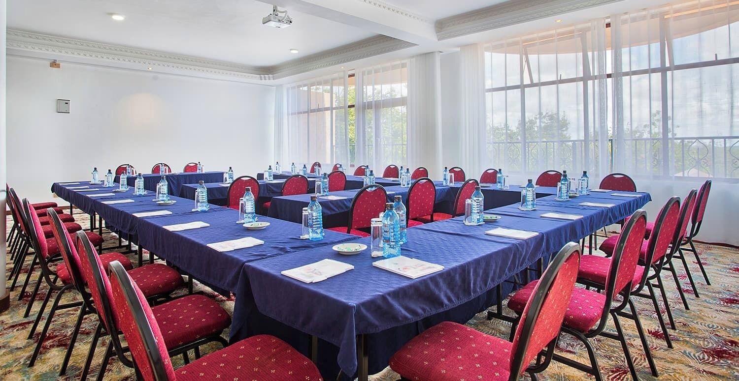 Ein Konferenzraum mit langen Tischen, roten Stühlen und Wasserflaschen.