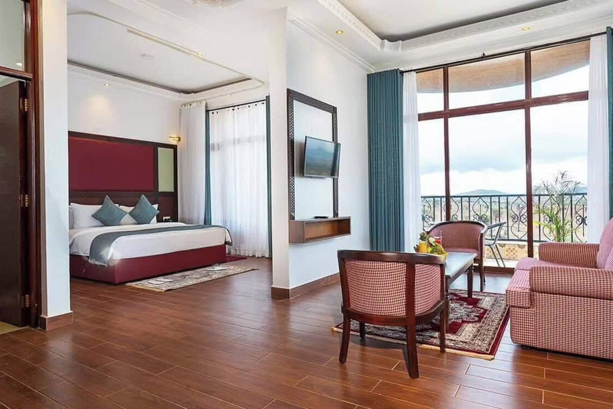Une chambre d’hôtel dotée d’un grand lit, d’un coin salon avec un canapé et des fauteuils, d’un balcon avec vue et d’un téléviseur fixé au mur.