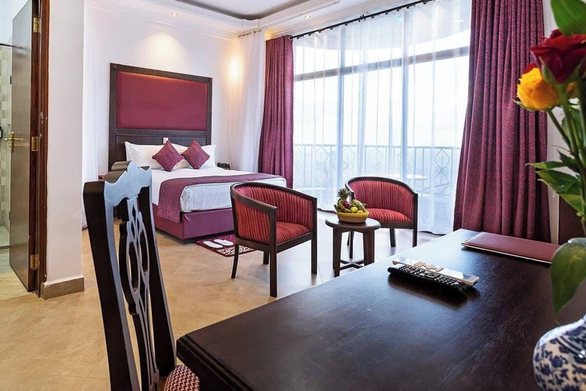 Une chambre d’hôtel avec un lit, un bureau, une chaise, une petite table et un vase avec des fleurs.