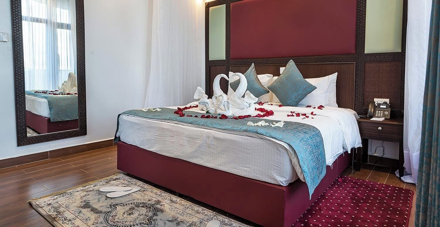 Une chambre d’hôtel avec un grand lit, une table de chevet, un miroir et un plancher en bois.