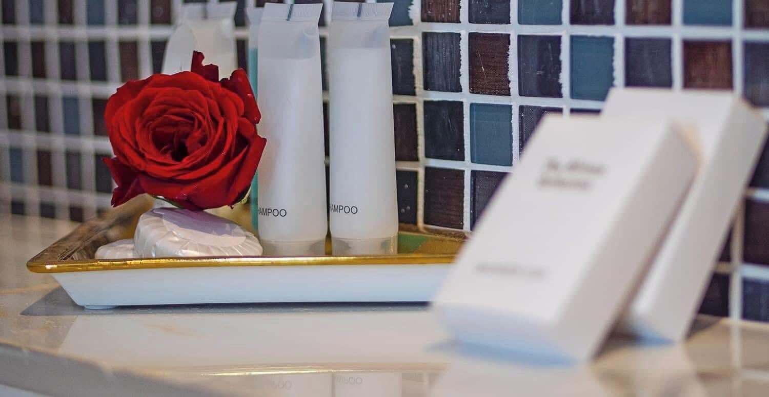 Un comptoir de salle de bain avec des articles de toilette, une rose rouge et un panneau.
