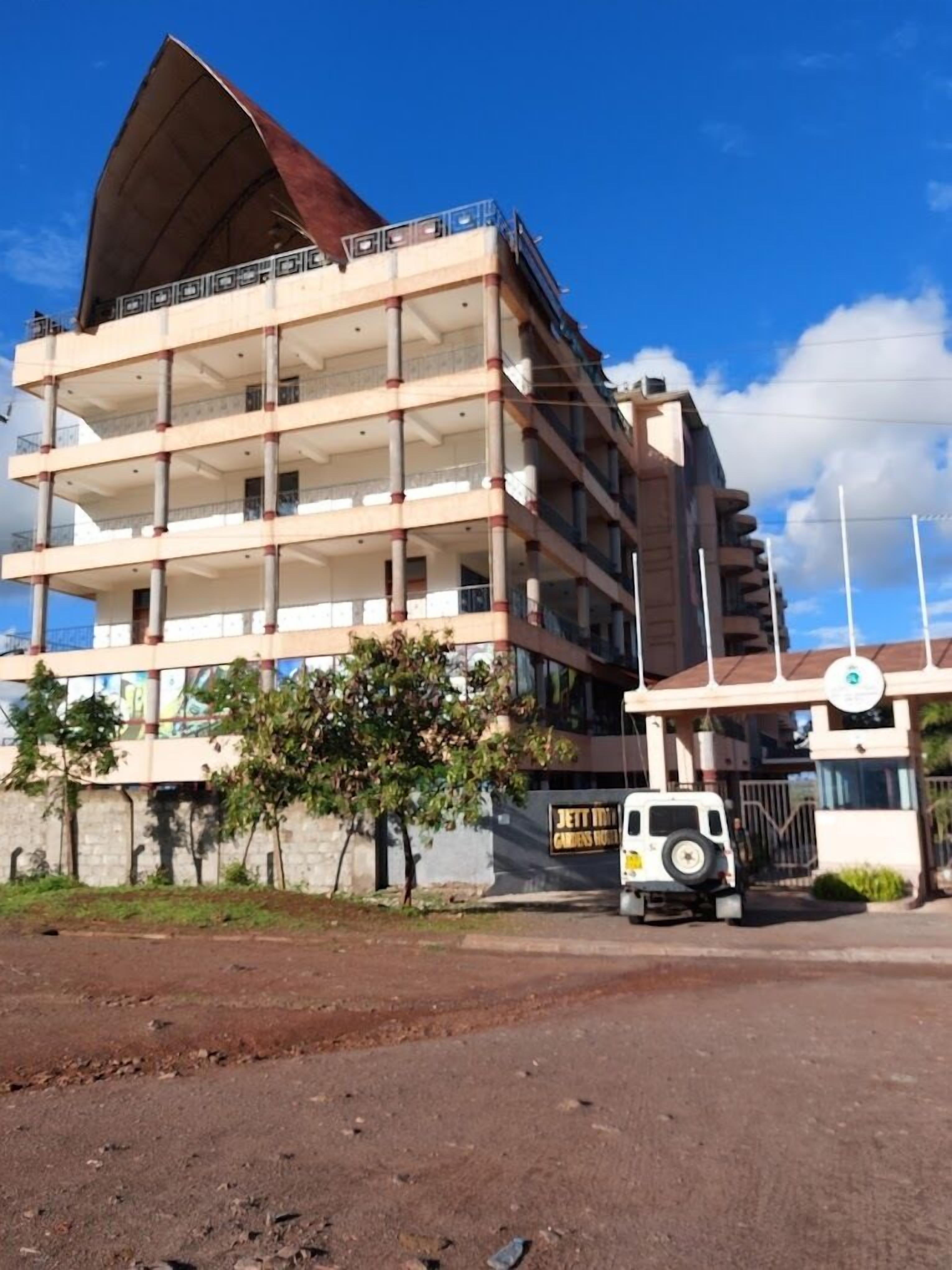 A multi-story building with a distinctive roof structure, a parking area with a white vehicle, and a sign indicating a garden hotel.