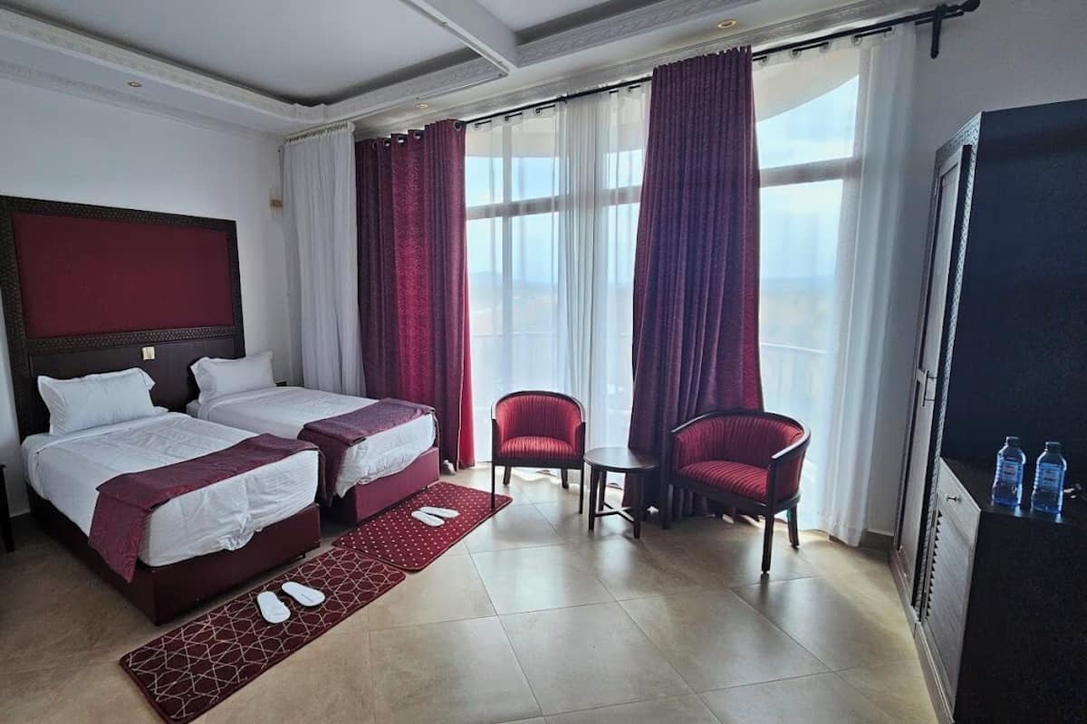 Une chambre d’hôtel avec deux lits, un coin salon avec un fauteuil et un minibar.