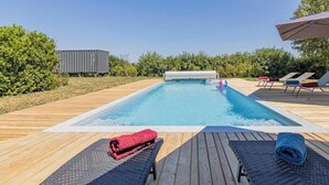 Una piscina con bordo in legno, sedie a sdraio e una zona coperta.