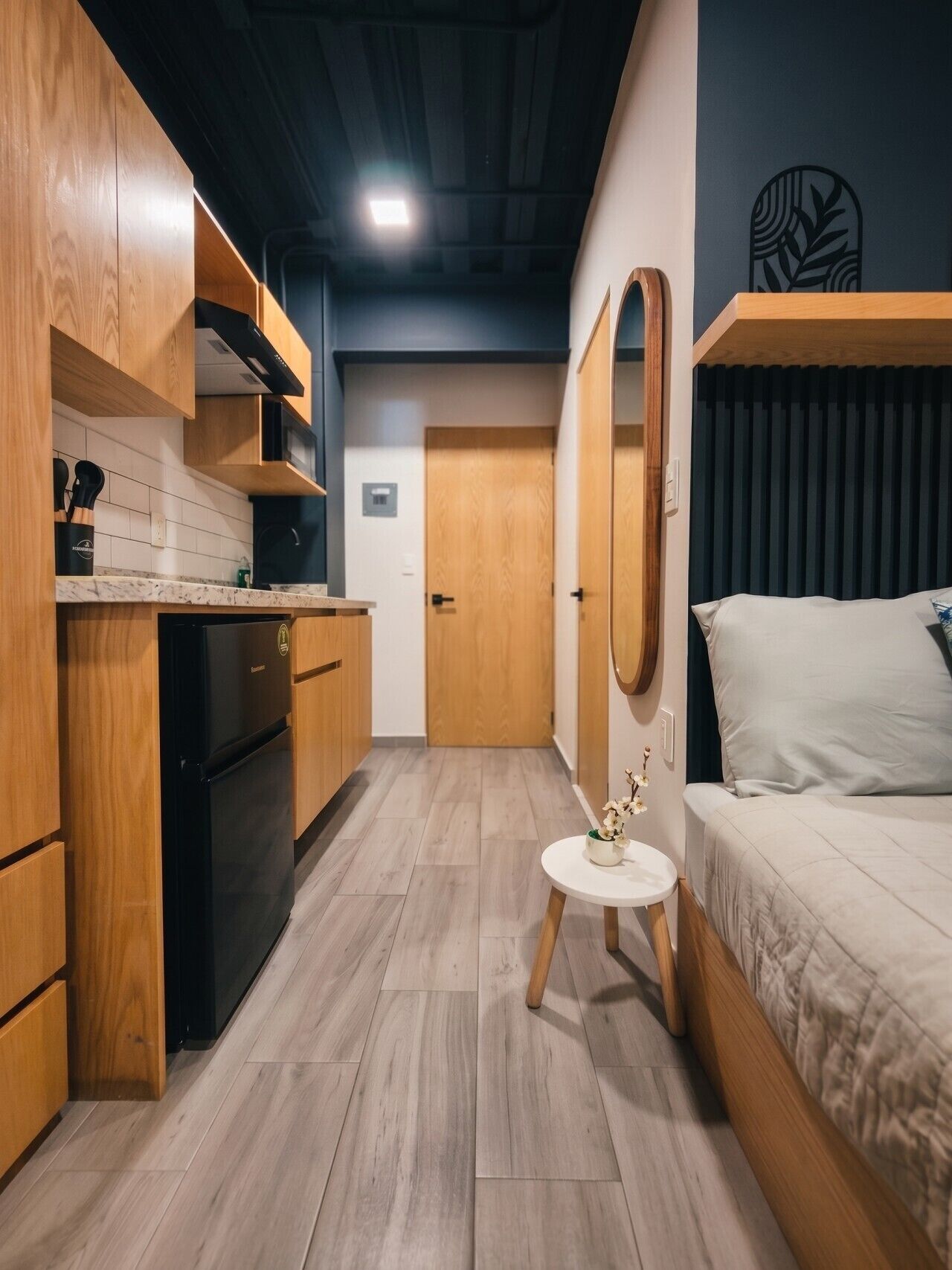 A compact room with a kitchenette, a bed, a small round table, and a mirror.