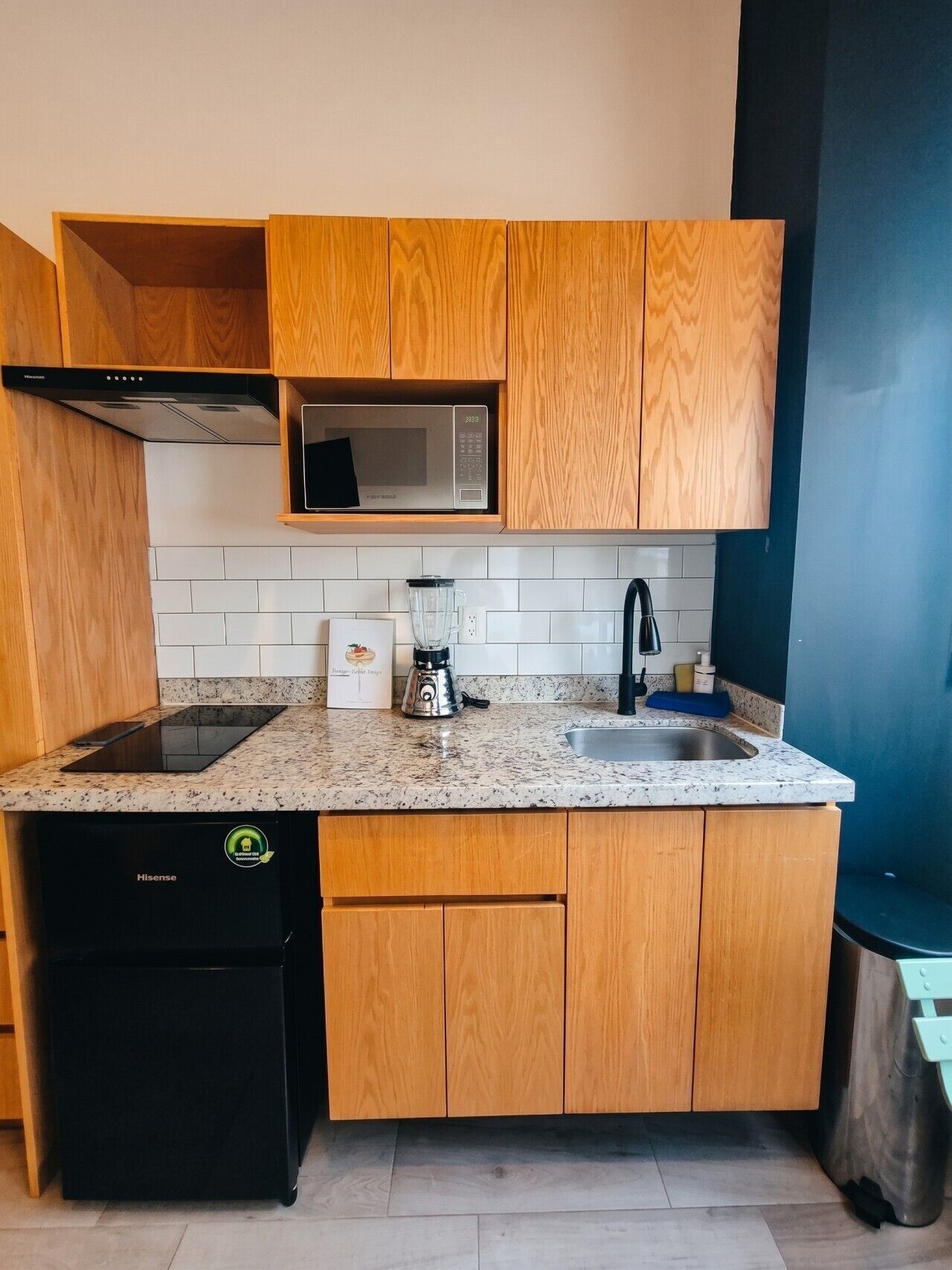 A compact kitchen with wooden cabinets, a microwave, a sink, a dishwasher, and a countertop with a blender.