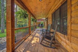 A wooden porch with rocking chairs, a railing, and a view of a forested area. - 4BR lake-access retreat with hot tub, pool table, dogs OK, and sleeps 11 (Oakland)