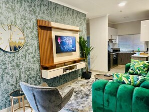 Un soggiorno moderno con una TV a schermo piatto montata su un pannello di legno, un divano verde, una poltrona grigia e un tappeto decorato.