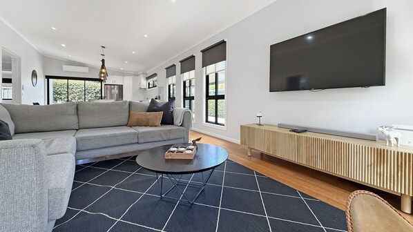 A modern living room with a sectional sofa, a round coffee table, a TV mounted on the wall, and a wooden console table. - Snowgum Bright Retreat - 2 Houses, 1 Location (Bright)