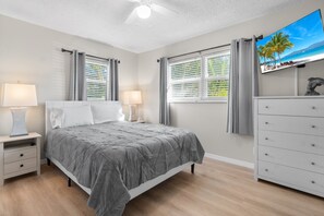 Quarto com cama, mesas de cabeceira, cômoda e televisão na parede.