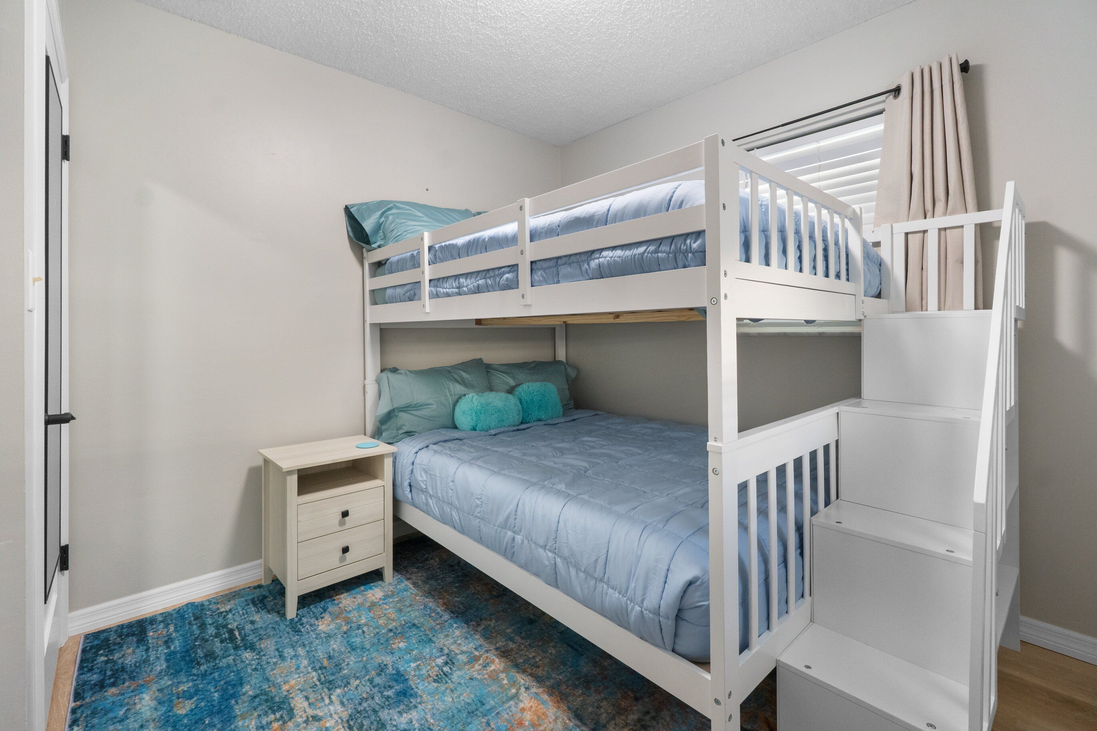 Une chambre avec un lit superposé, une petite table de chevet et un tapis bleu à motifs.