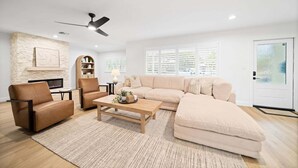 A living room with a sectional sofa, a leather armchair, a wooden coffee table, a fireplace, and a ceiling fan. - 114 Managed by Brampton Park (Delray Beach)