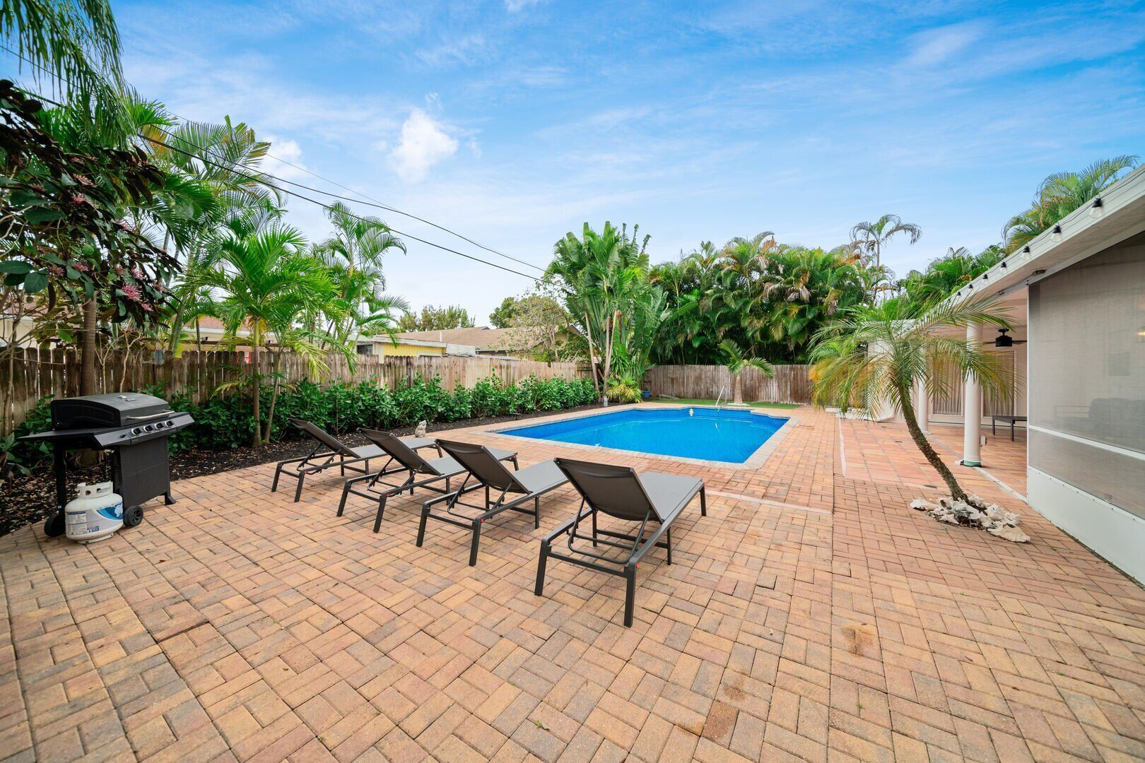 A backyard with a swimming pool, lounge chairs, a barbecue grill, and a brick patio.