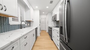 A modern kitchen with white cabinetry, a stainless steel refrigerator, and a herringbone-patterned backsplash. - 114 Managed by Brampton Park (Delray Beach)
