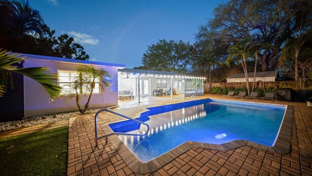 A swimming pool with a brick deck, a covered patio area, and a small house with a porch. - 114 Managed by Brampton Park (Delray Beach)