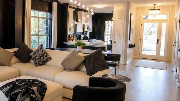 A modern living room with a sectional sofa, a black ottoman, and a patterned rug. - McConnell Golf Retreat Near Sedgefield Country Club (Greensboro)