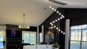 A modern living room with a black and white color scheme, a fireplace, a dining area with a round table and chairs, and a large window providing natural light. - McConnell Golf Retreat Near Sedgefield Country Club (Greensboro)