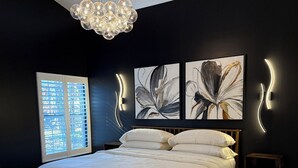 A bedroom with a large bed, a chandelier, abstract wall art, and a window with blinds. - McConnell Golf Retreat Near Sedgefield Country Club (Greensboro)