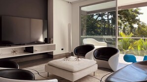 A modern living room with a flat-screen TV, a sofa, and two chairs.