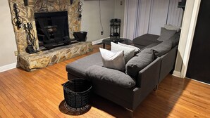 A living room with a stone fireplace, a grey sofa, and a television mounted on the wall. - Fully Furnished 3BR Home • Fast Wi-Fi • Parking • Near Uptown (Charlotte)