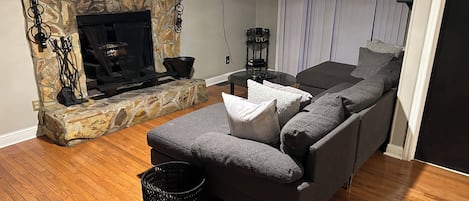 A living room with a stone fireplace, a grey sofa, and a television mounted on the wall.