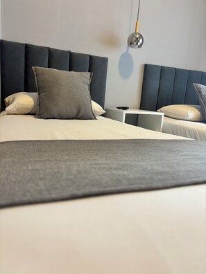 A neatly made bed with a grey headboard, a bedside table with a lamp, and a wall-mounted light fixture.