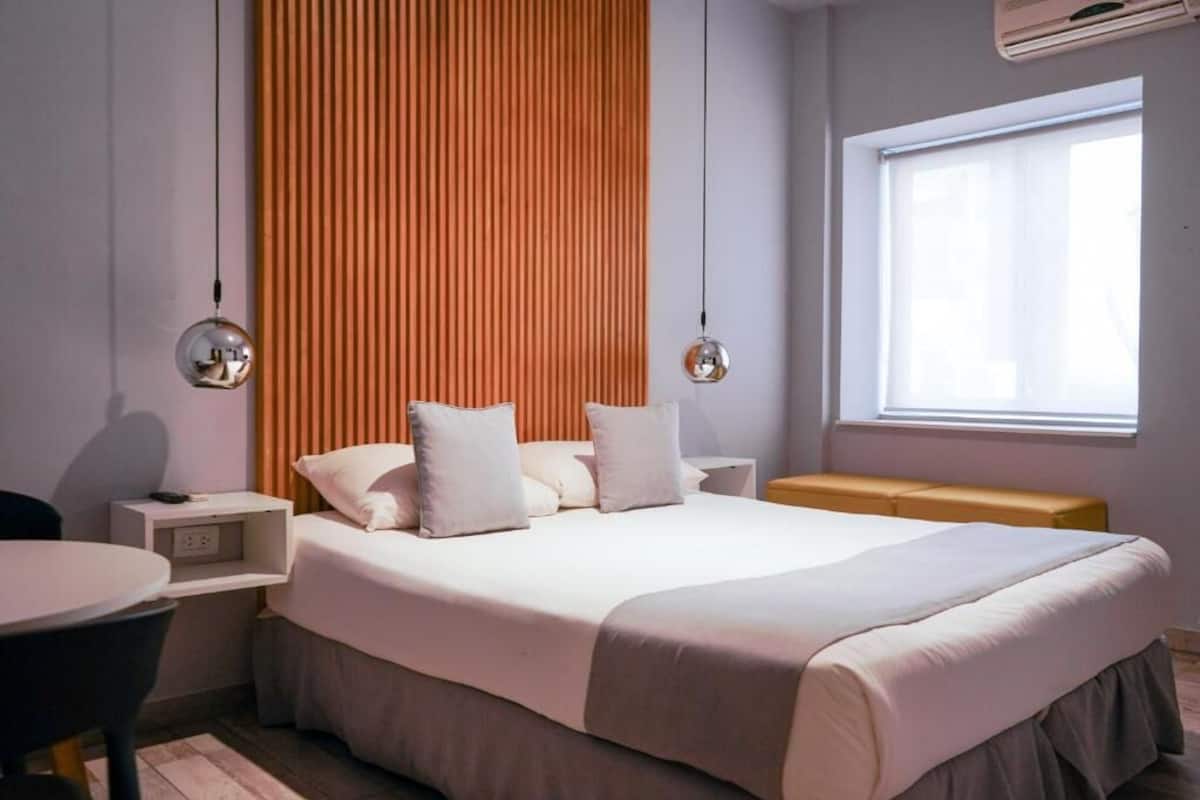 Quarto moderno com cama grande, mesas de cabeceira, um banco e uma janela.