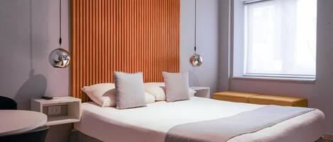 Un dormitorio moderno con una cama grande, mesitas de noche, un banco y una ventana.