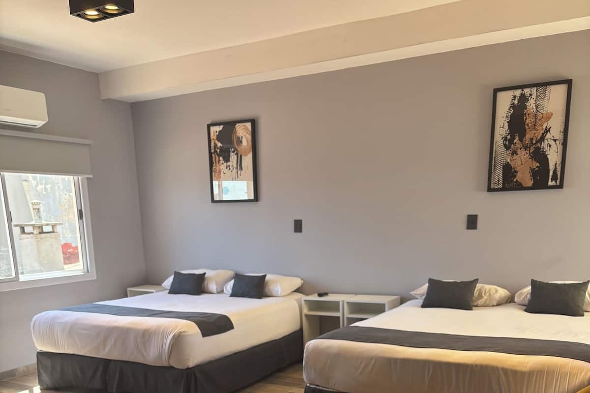 Quarto de hotel com duas camas, uma mesinha e obras de arte nas paredes.