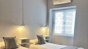 Een hotelkamer met twee bedden, nachtkastjes, een raam en een wandairconditioner.