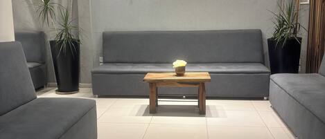 Een moderne woonkamer met een grijze bank, een houten salontafel en potplanten.