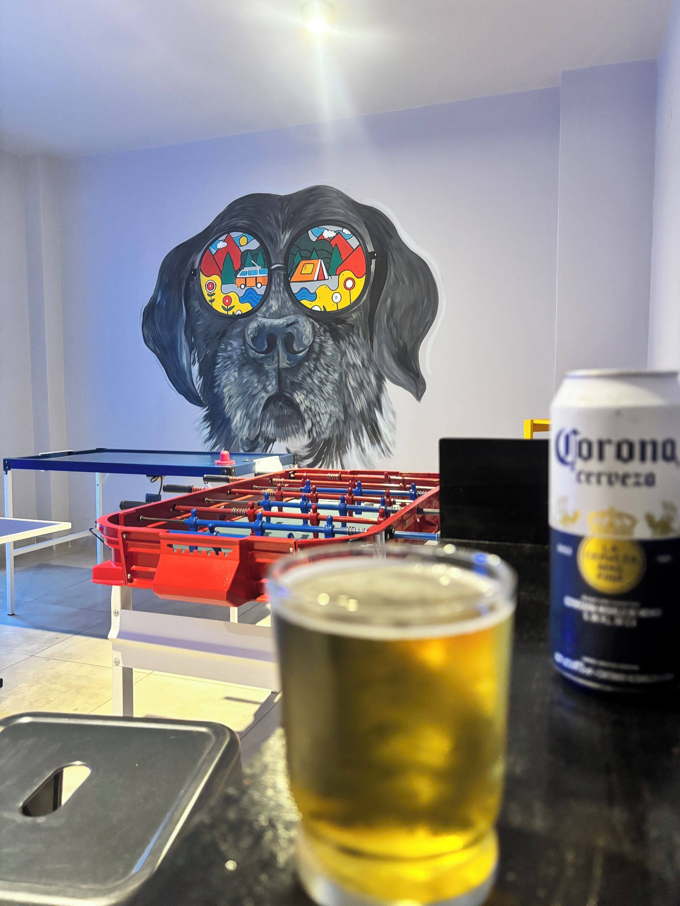 Ein Kicker, ein Bierglas und eine Corona-Dose auf einer Tischplatte.