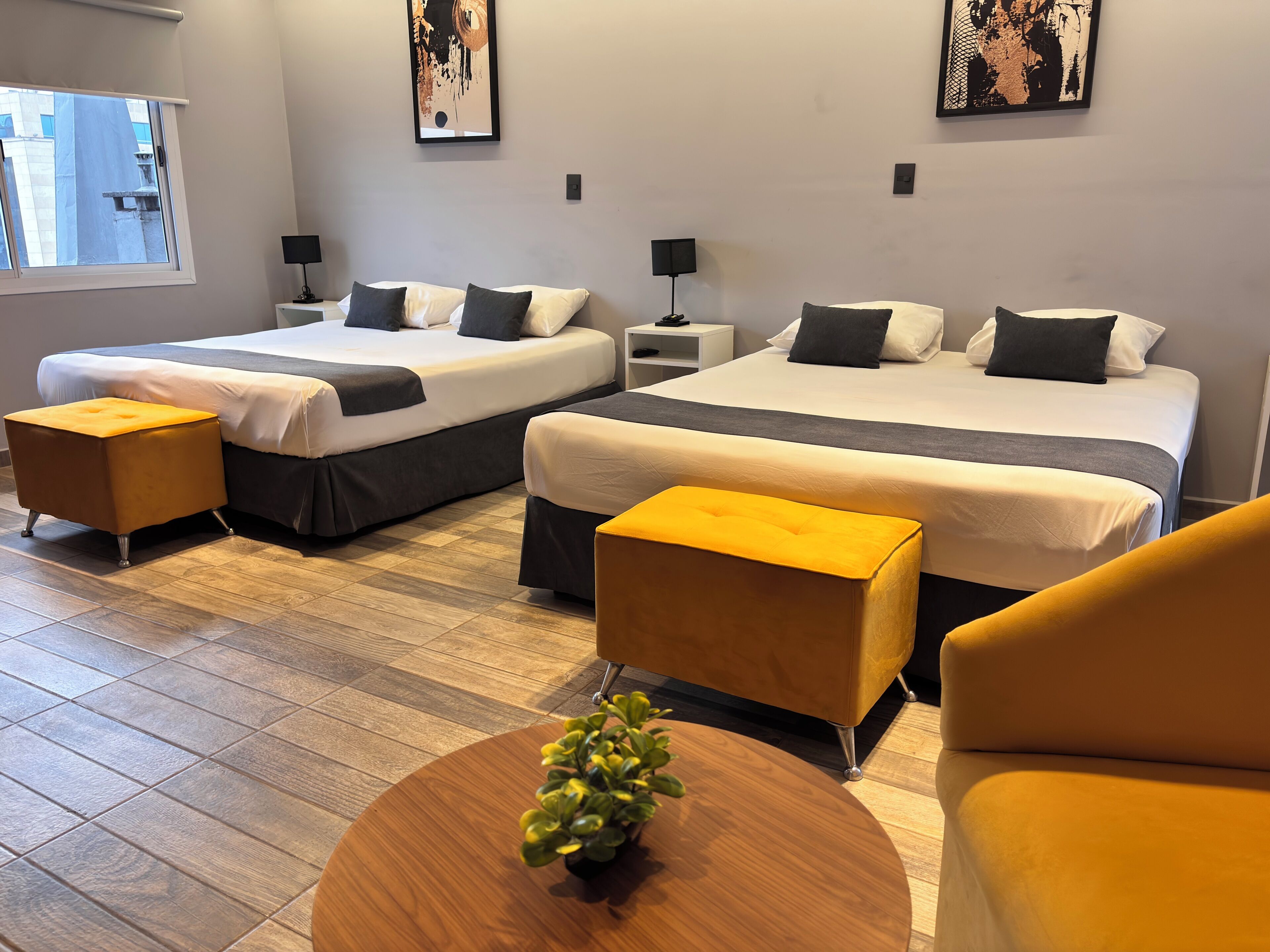 Una habitación de hotel con dos camas, una mesita con una planta y un sillón amarillo.